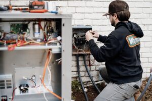 An HVAC technician connecting wiring to an outdoor electrical panel for Wingman Heating + Cooling in Auburn, AL.