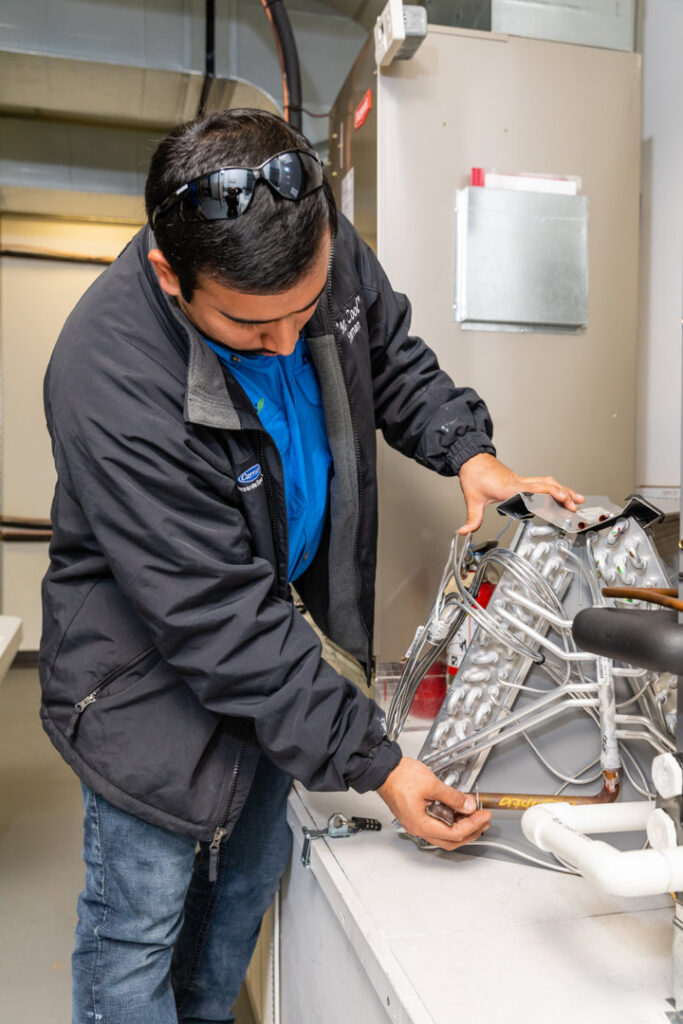 An HVAC technician from Mr. Cool HVAC working on an evaporator coil or heat exchanger component in Cypress, TX.