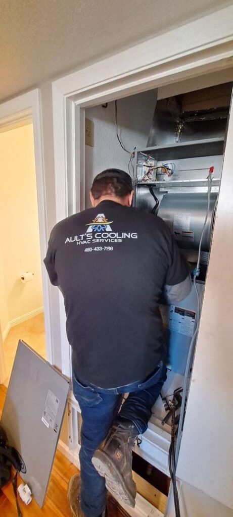 An HVAC technician from Ault's Cooling HVAC Services LLC working on an indoor furnace or air handler unit in Chandler, AZ.
