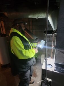 An HVAC technician working on a furnace, holding a piece of ductwork or component, for Family First Heating and Cooling Repair LLC in Toledo, OH.