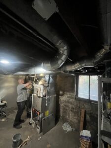 An HVAC technician from JM HVAC Pros working on a furnace and ductwork in a basement in Elgin, IL.