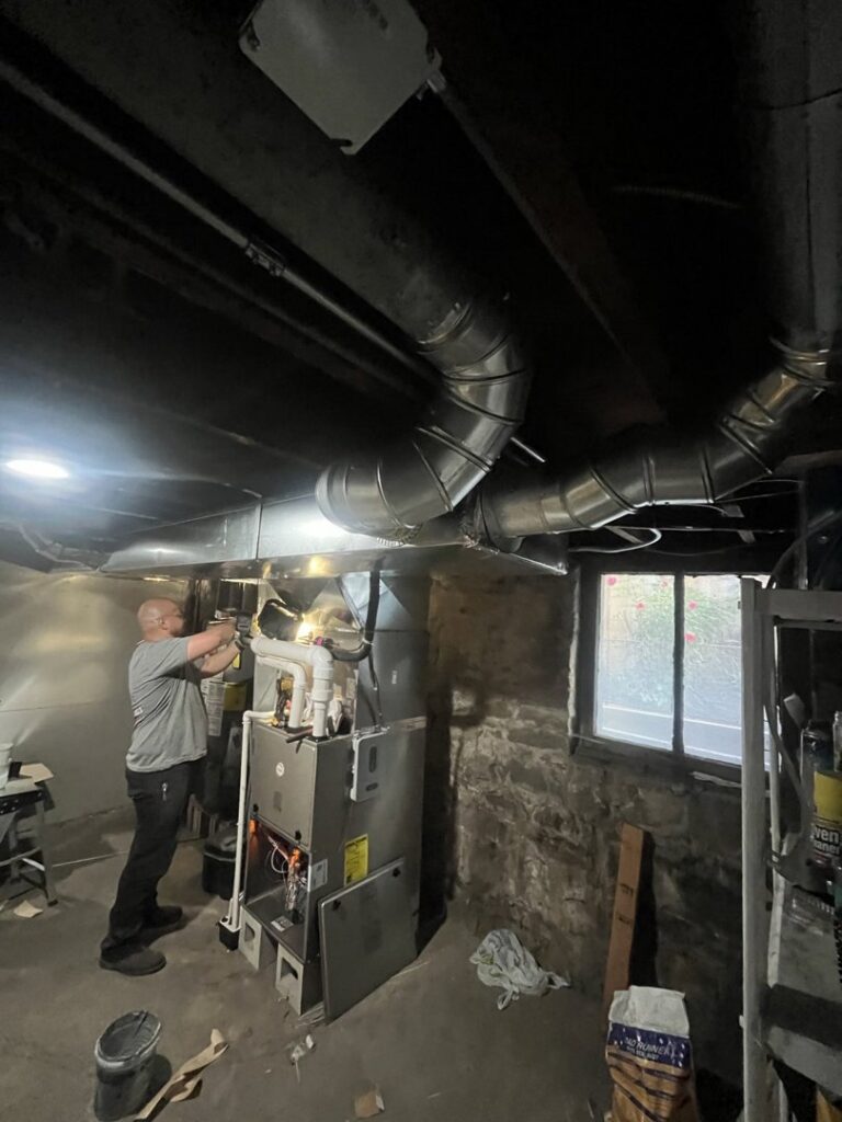 An HVAC technician from JM HVAC Pros working on a furnace and ductwork in a basement in Elgin, IL.