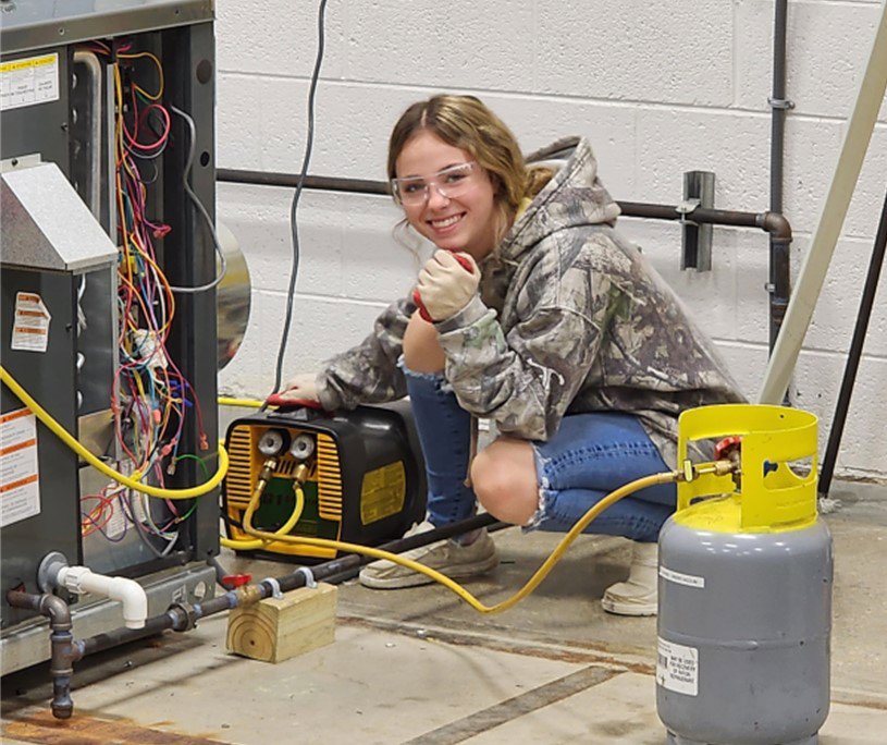 A skilled HVAC technician working on an open furnace unit with a refrigerant tank, provided by Joe Logan HVAC in Dayton, OH.