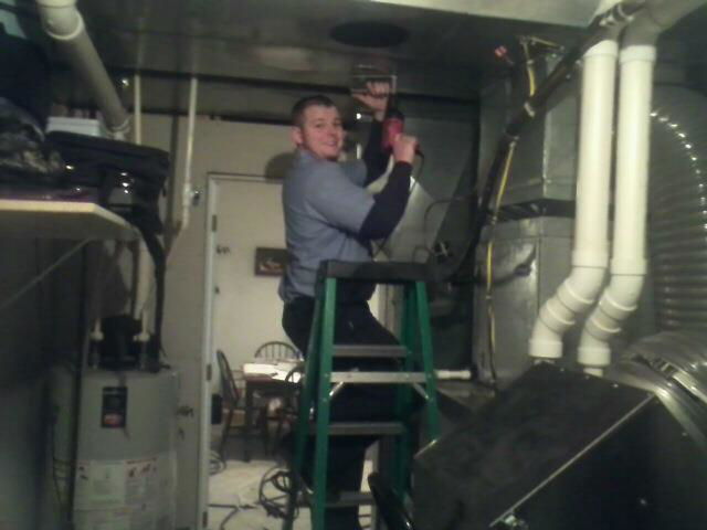 An HVAC technician working on a furnace or ductwork in a utility room for Midwest Air Solutions in Indianapolis, IN