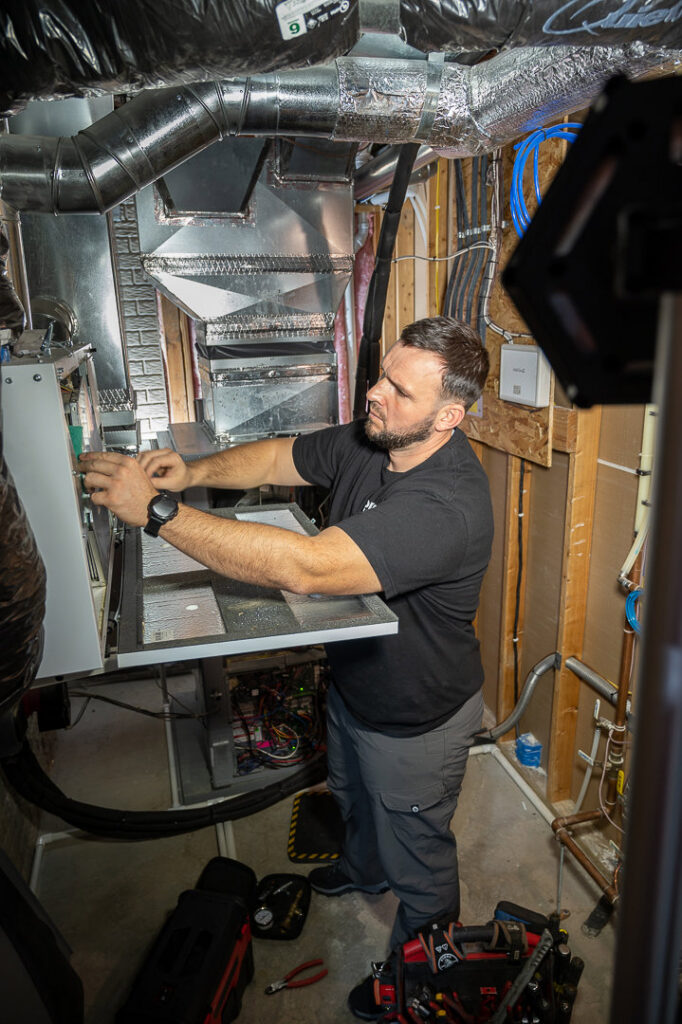 An HVAC technician from Omega Air Solutions working on an indoor furnace unit in West Des Moines, IA.