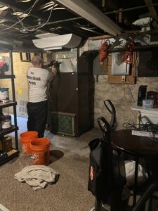 An HVAC technician from One Hour Heating & Air Conditioning of Lancaster, PA, working on a furnace in a residential basement.