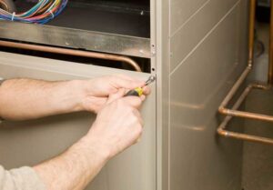 An HVAC technician's hands using a screwdriver to work on a furnace or air handler panel for NorthStar Services in South Haven, MN