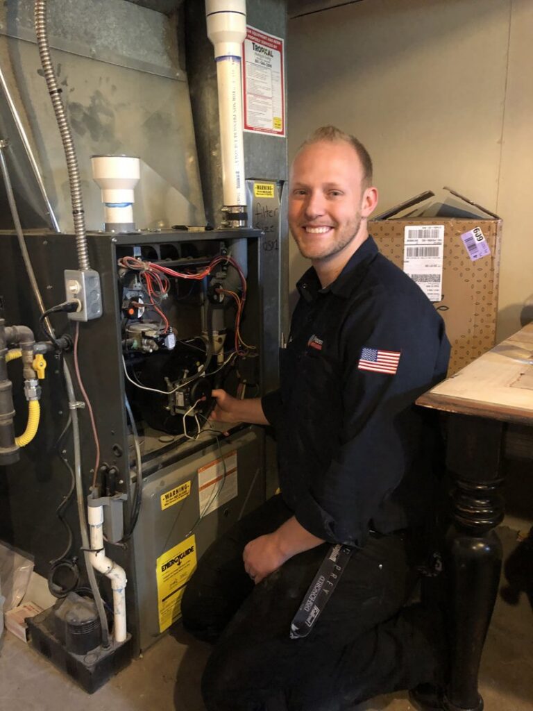 A Peterson Heating & Cooling technician kneeling and working on an open furnace unit during a service call in Mound City, KS.