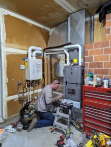 An HVAC technician performing work on a furnace and tankless water heater system for Gresham Heating and Air Conditioning in Wood Village, OR.
