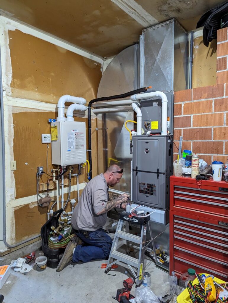 An HVAC technician performing work on a furnace and tankless water heater system for Gresham Heating and Air Conditioning in Wood Village, OR.