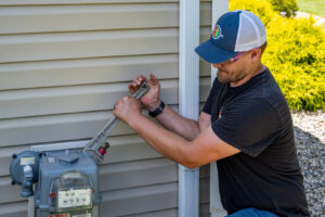 An HVAC technician from Comfort Craftsman Heating & Cooling working on a gas meter outside a home in Westland, MI.