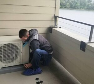 An HVAC technician working on an outdoor heat pump unit installed on a residential balcony by The Heat Pump Store in Portland, OR.