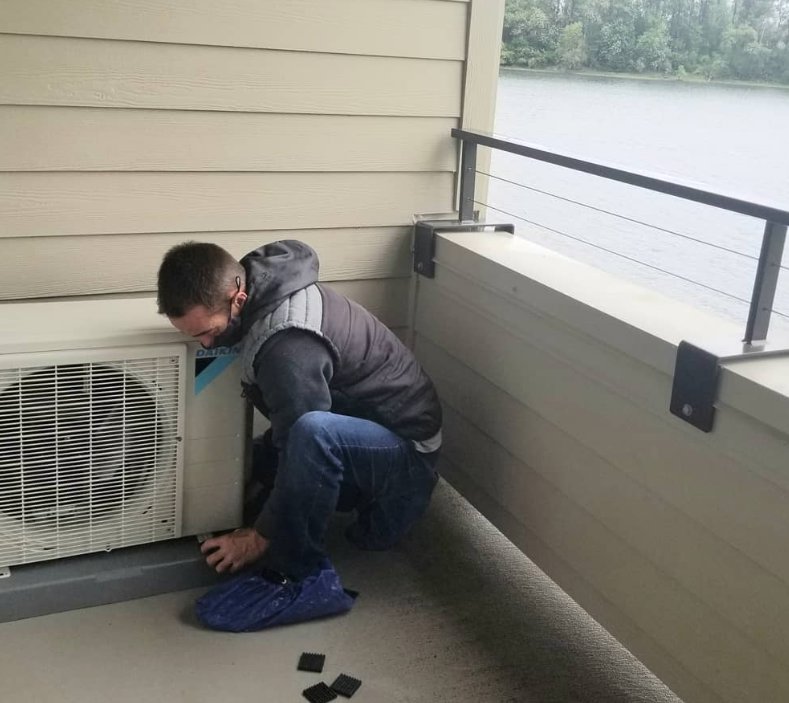 An HVAC technician working on an outdoor heat pump unit installed on a residential balcony by The Heat Pump Store in Portland, OR.