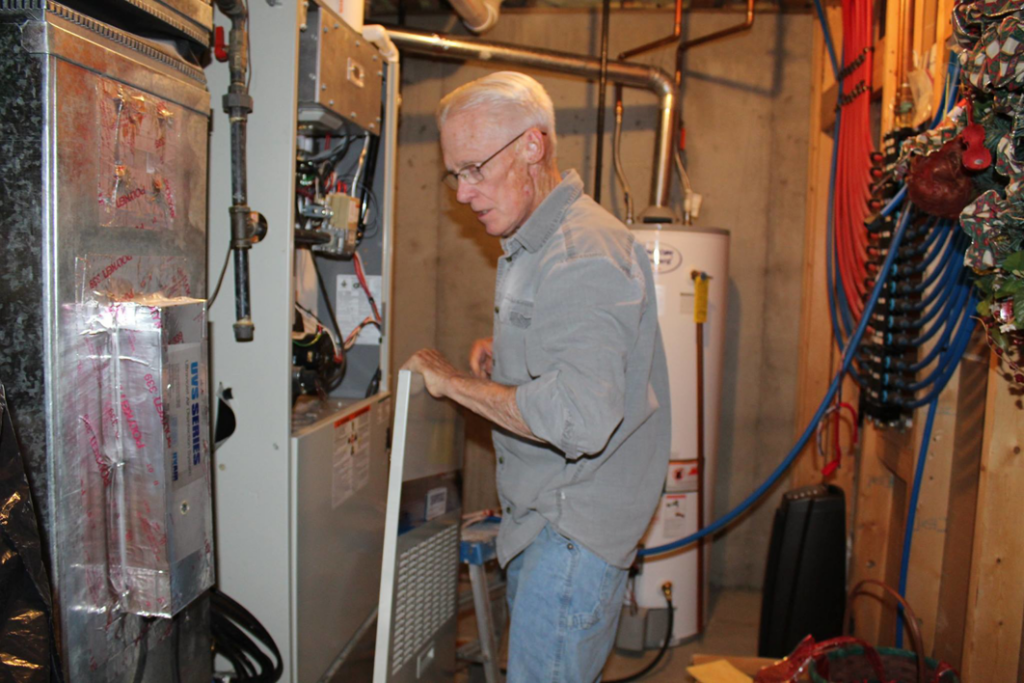 An HVAC technician working on an indoor heating and air conditioning unit in a utility room for West Wichita Heating & Air Conditioning in Wichita, KS.