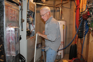 An HVAC technician working on an indoor heating and air conditioning unit in a utility room for West Wichita Heating & Air Conditioning in Wichita, KS.