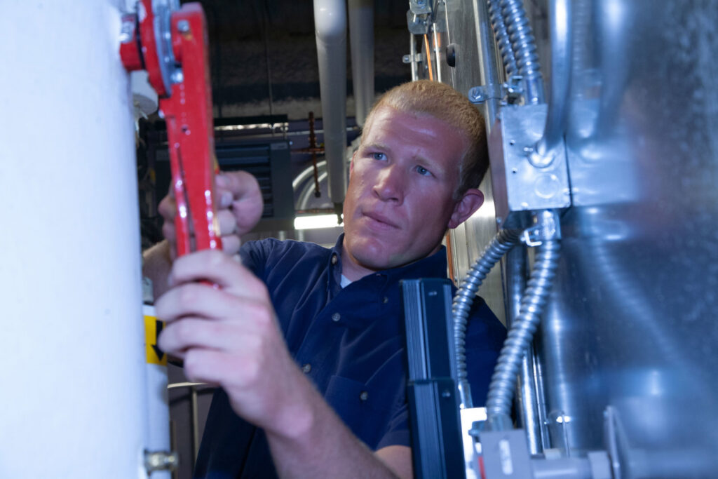 An HVAC technician working on pipes and controls in an indoor mechanical room for Climate Systems, Inc. in Sioux Falls, SD.