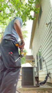 An HVAC technician using a drill while working on an outdoor AC unit for Airtegrity Comfort Solutions in San Antonio, TX