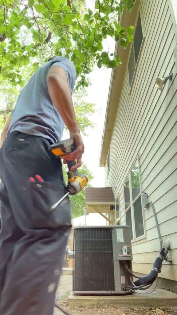 An HVAC technician using a drill while working on an outdoor AC unit for Airtegrity Comfort Solutions in San Antonio, TX