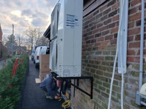 An HVAC technician working on an outdoor mini-split unit mounted on a brick wall for Aces of Air Inc. in Georgetown, KY.