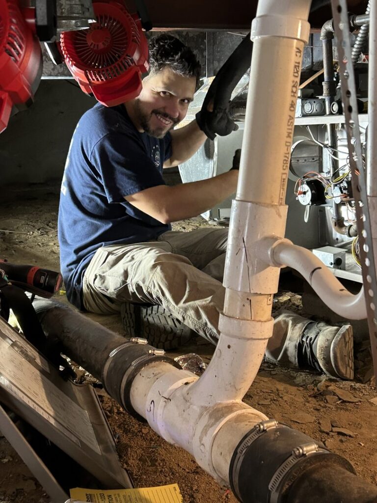 A Sandys Heating & Air technician working on pipes and wiring in a utility area in Papillion, NE.