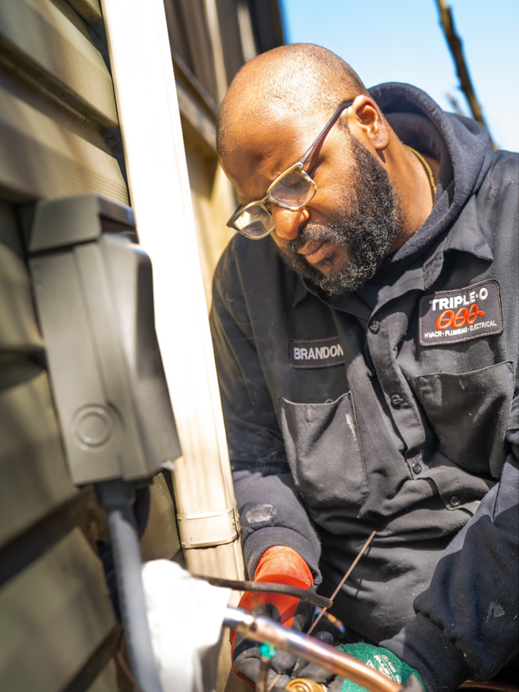 An HVAC technician from Triple-O working on copper refrigerant lines for an outdoor unit in Bergen, NY.