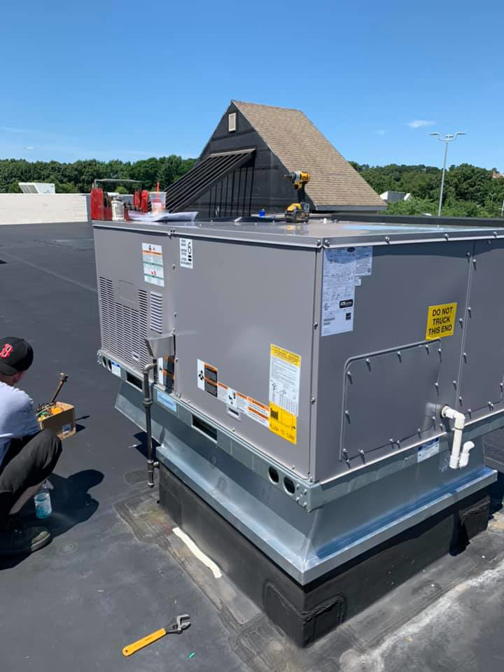 An HVAC technician working on a commercial rooftop unit installation for Air Quality, LLC in Cranston, RI