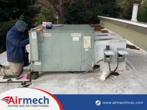 An Airmech Heating and Air Conditioning technician performing service on a commercial rooftop HVAC unit in Elk Grove, CA.