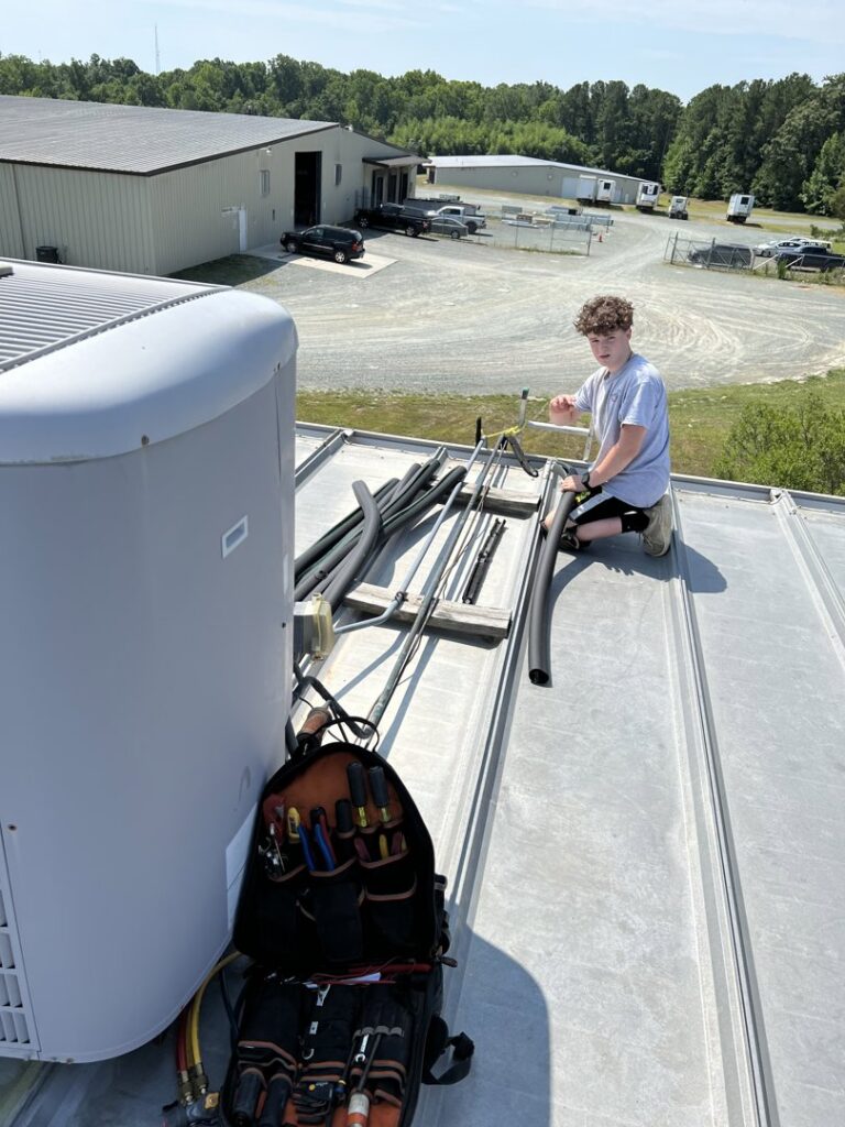 An HVAC technician working on a rooftop air conditioning unit and refrigerant lines for Workman Mechanical in Graham, NC.