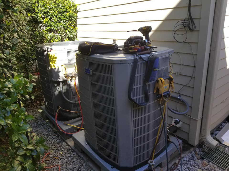 An HVAC technician working on two outdoor air conditioning units with tools at Comfort Zone A/C & Heating, LLC in Kenner, LA.