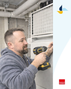 An HVAC technician using a drill to work on a large indoor HVAC unit for Climate Systems, Inc. in Sioux Falls, SD.