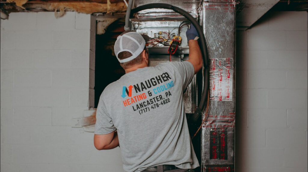 An HVAC technician from Naugher Heating and Cooling working on an indoor unit with a multimeter in Lancaster, PA