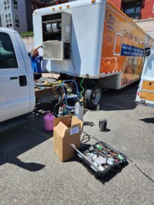 An HVAC technician working on an outdoor unit mounted on a trailer, surrounded by tools, for Thin Air Heating and Cooling in Arvada, CO.
