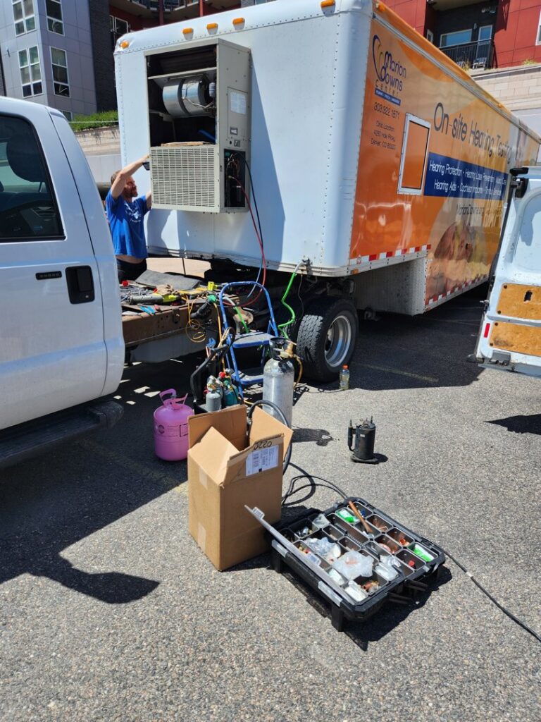 An HVAC technician working on an outdoor unit mounted on a trailer, surrounded by tools, for Thin Air Heating and Cooling in Arvada, CO.