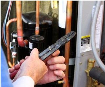 A close-up of an HVAC technician's hands using a tool to work on wiring near an outdoor unit's components for KATS Heating & Cooling in La Grange Park, IL.