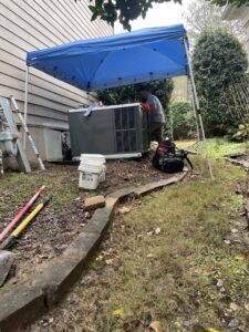 An HVAC technician working on an outdoor unit under a blue canopy for Luciano's Air Services in Durham, NC.