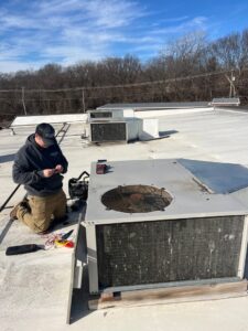An HVAC technician from Pro-Cool Air Conditioning & Heating performing service on a commercial rooftop unit in Blue Springs, MO.