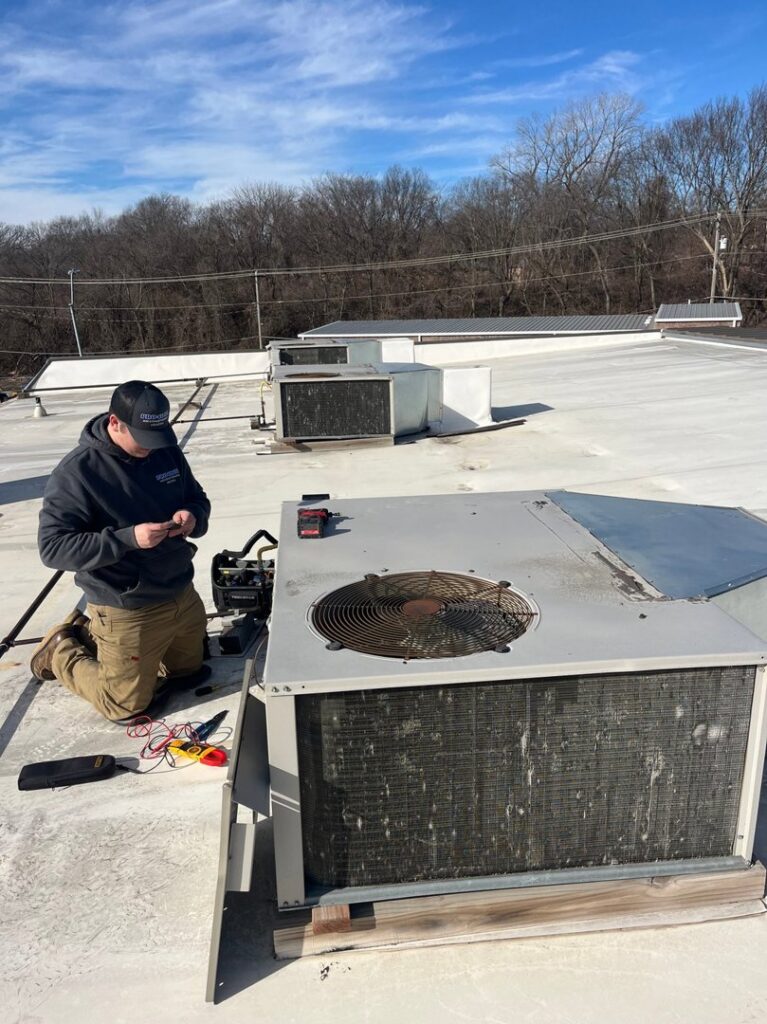 An HVAC technician from Pro-Cool Air Conditioning & Heating performing service on a commercial rooftop unit in Blue Springs, MO.