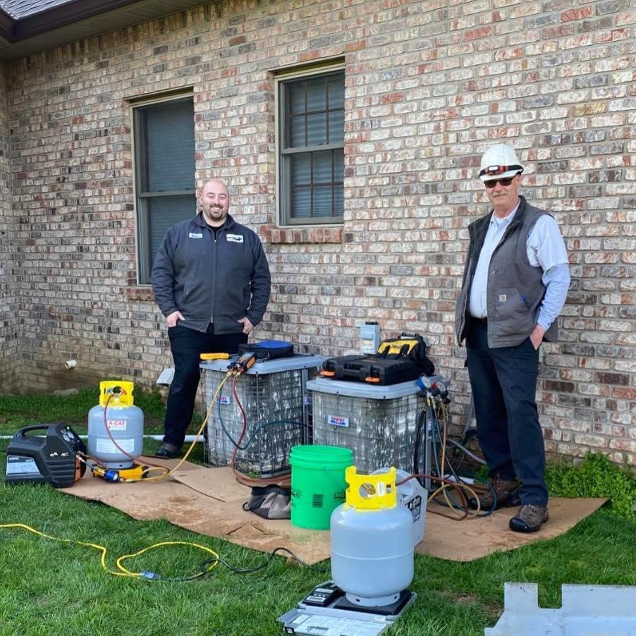 HVAC technicians performing AC service or repair with tools and refrigerant tanks for Roy Rogers Heating and Air in Indianapolis, IN.