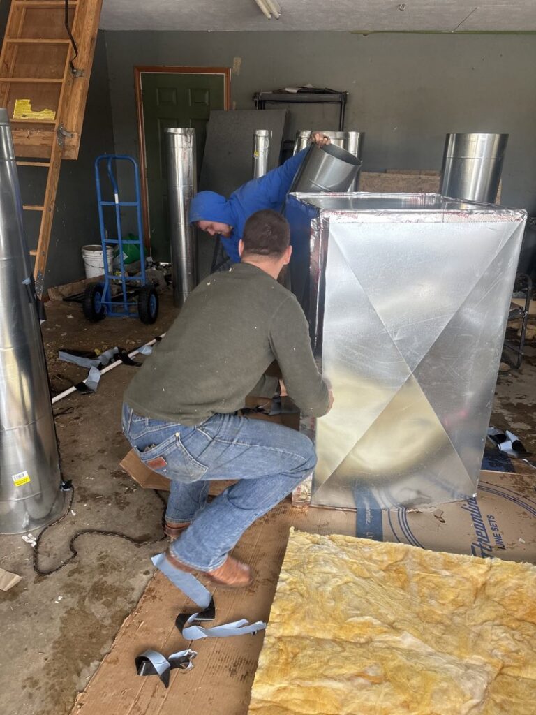 Two HVAC technicians assembling sheet metal ductwork in a workshop for Dewees HVAC in Conway, AR.