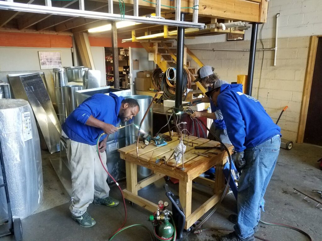 Two Air Specialty Heating & Air Conditioning technicians brazing copper pipes for an HVAC installation in Norfolk, VA.