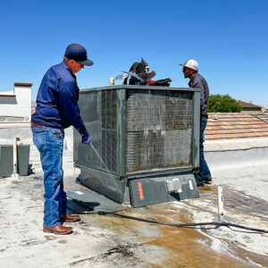 Two HVAC technicians cleaning a rooftop air conditioning unit during maintenance by EA Heating & Cooling in El Paso, TX.