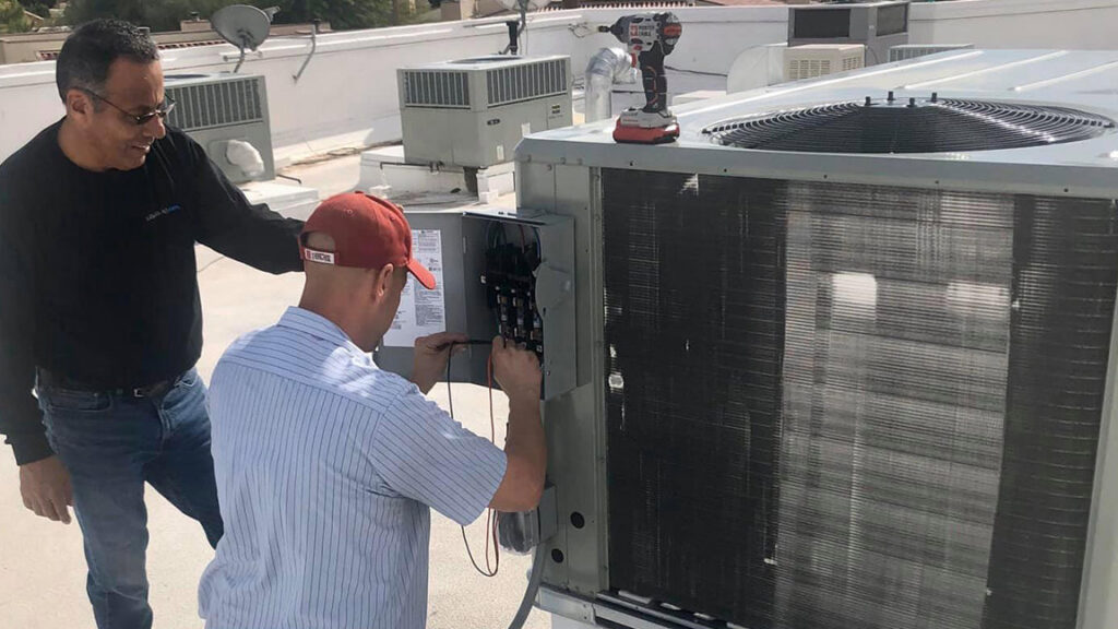 Two Lincoln Air & Plumbing technicians diagnosing a rooftop HVAC unit with a multimeter in Phoenix, AZ