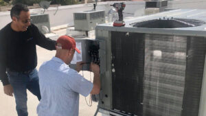Two Lincoln Air & Plumbing technicians diagnosing a rooftop HVAC unit with a multimeter in Phoenix, AZ