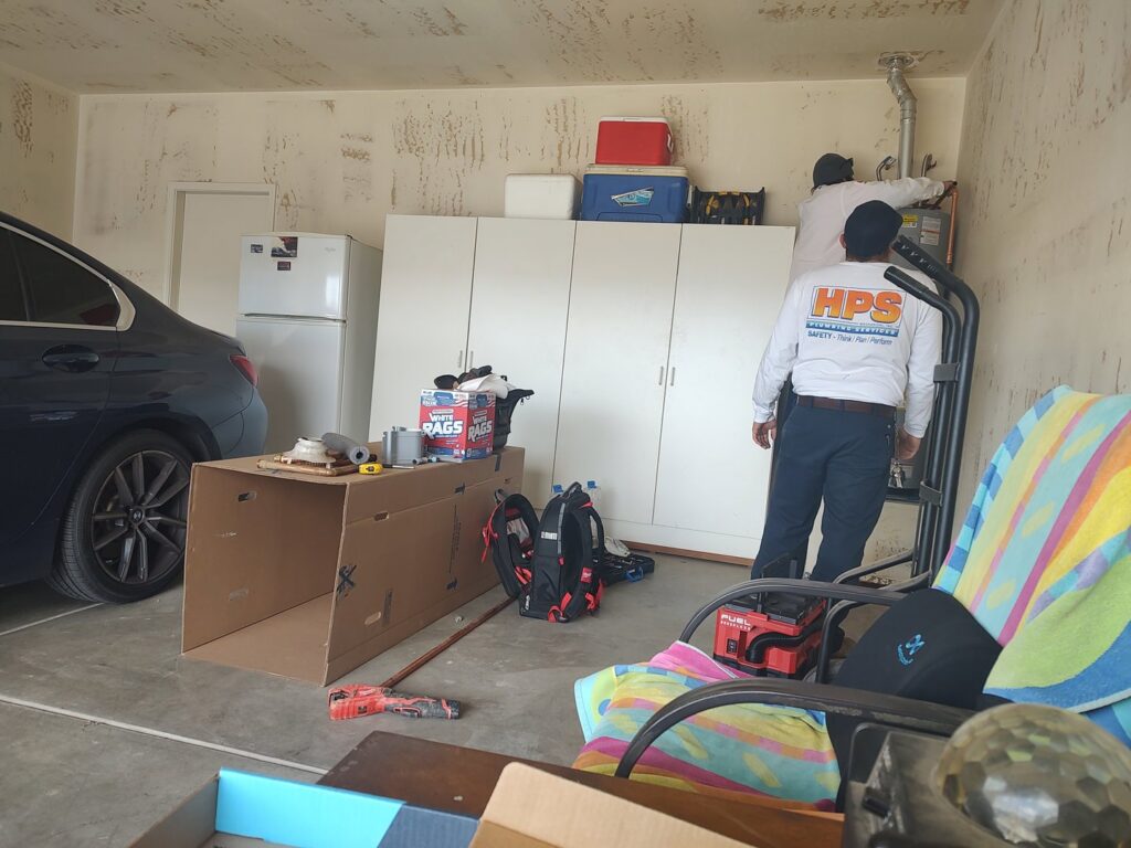 HVAC technicians installing a furnace or air handler in a garage for HPS Plumbing Services Bakersfield, CA.