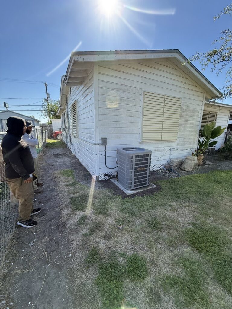 Two HVAC technicians from Gibson's Air Conditioning & Heating inspecting an outdoor AC unit at a residential property in Corpus Christi, TX.