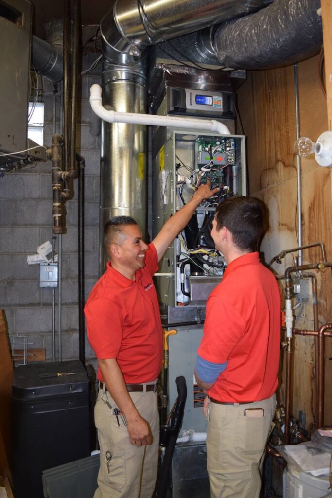 Two HVAC technicians from Family Heating & Air Conditioning inspecting a furnace in Indianapolis, IN.