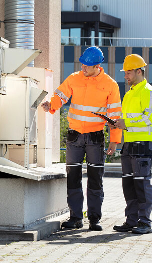 Two HVAC technicians in hard hats inspecting an outdoor commercial HVAC unit for Accurate Air Inc. in Manchester, NH.