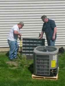 Two HVAC technicians installing an outdoor air conditioning unit for a client at Affordable Services Heating and Air Conditioning Inc. in Aurora, IL