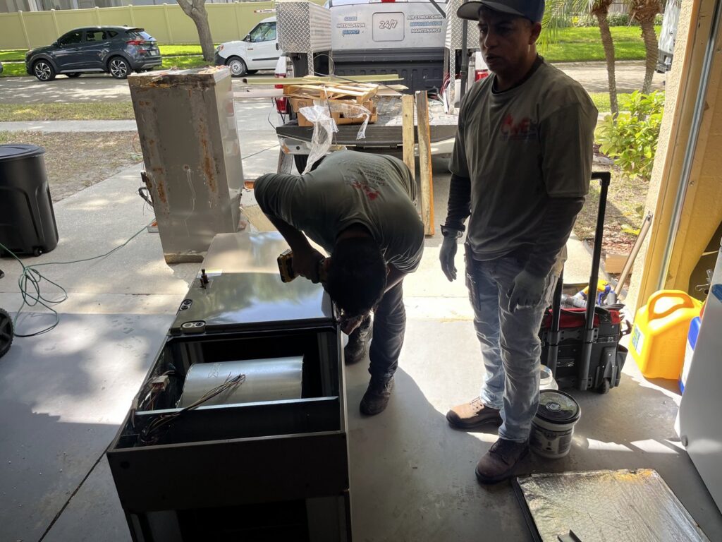 Two HVAC technicians installing an air handler unit in a garage for Timely Air Conditioning in Riverview, FL.