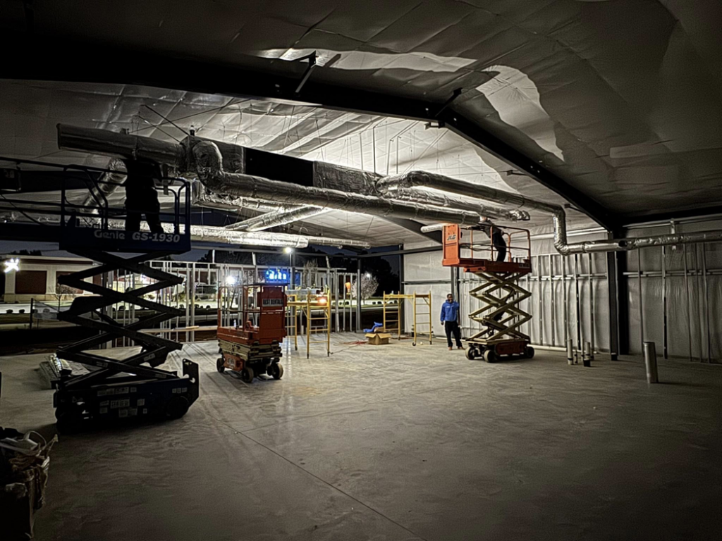 HVAC technicians installing insulated ductwork on scissor lifts at night for Delta Heating, Cooling, Plumbing in Wilson, NC.